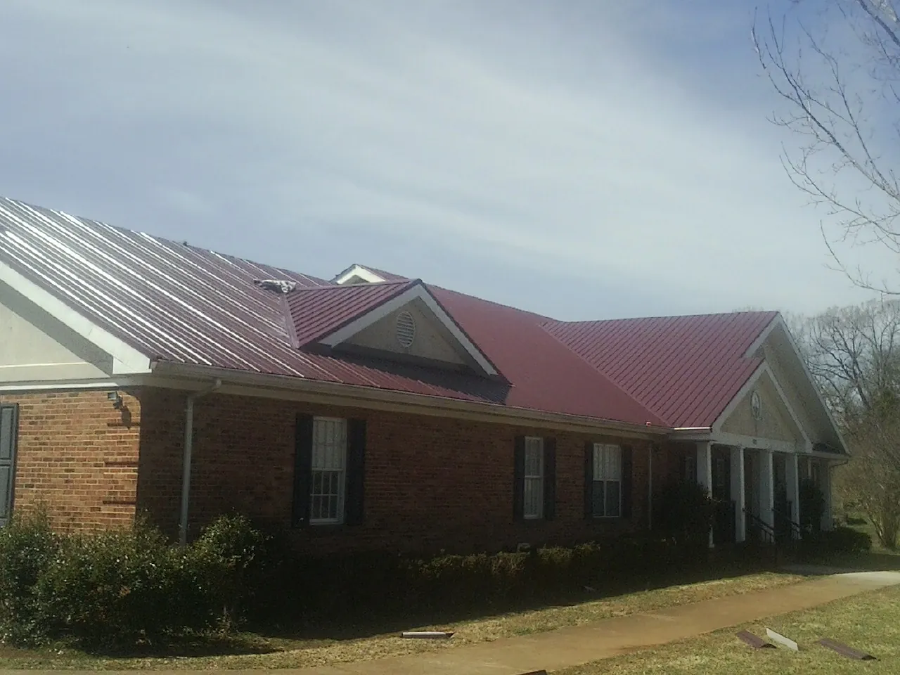 Red metal roof with gabled entries on a long brick building, from a Hail Damage Roof Repair job in Hilliard